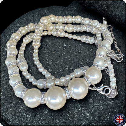 A multi-strand pearl beaded necklace with silver-toned spacer beads and a lobster clasp, displayed on a dark textured rock background.