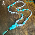 A close-up, detailed image of the turquoise beaded necklace showing polished turquoise nuggets combined with luminous pearl beads and silver rhinestone separators. The handcrafted jewellery design reveals natural turquoise veining and glossy pearl reflections against the wooden surface. The sterling silver findings add elegance while the long silhouette gives a timeless bohemian style appearance suitable for daily wear or special occasions.