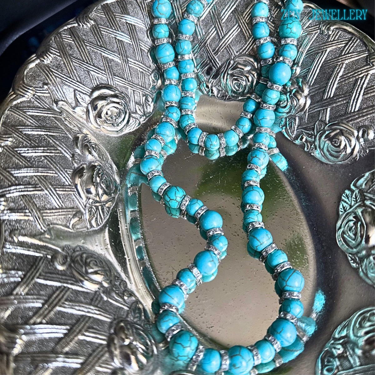 This handcrafted turquoise and silver jewellery set features matching necklace and bracelet pieces with smooth turquoise beads in varying sizes, displayed on a silver plate. Rhinestone accents add subtle elegance while the rich blue-green gemstone tones create a luxurious, vintage, elegant-inspired look suitable for everyday styling or gift-giving occasions.