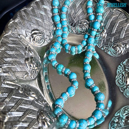 This handcrafted turquoise and silver jewellery set features matching necklace and bracelet pieces with smooth turquoise beads in varying sizes, displayed on a silver plate. Rhinestone accents add subtle elegance while the rich blue-green gemstone tones create a luxurious, vintage, elegant-inspired look suitable for everyday styling or gift-giving occasions.