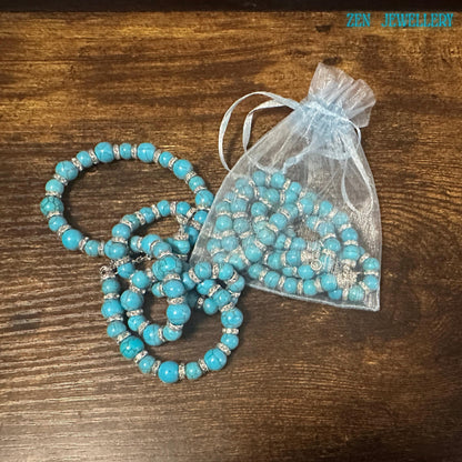 The handmade turquoise beaded necklace and bracelet set is displayed on dark rustic wood to emphasise the rich gemstone colours and polished bead textures. Round turquoise stones with natural marbling patterns are paired with rhinestone spacer beads, creating a sophisticated bohemian style jewellery appearance. Elegant turquoise rhinestone necklace displayed in a jewellery gift pouch.
