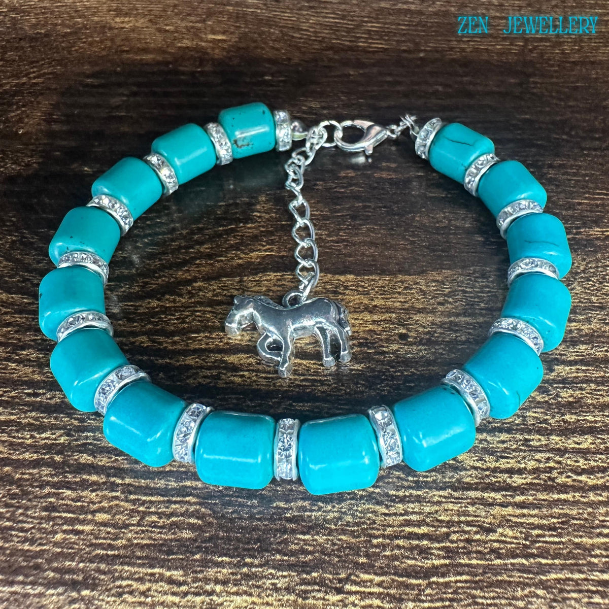 Turquoise tube bead bracelet with sparkly rhinestone spacers and a silver horse charm. Vibrant blue stones and silver extender chain shown against a wooden background. Bracelet displayed on a wood table