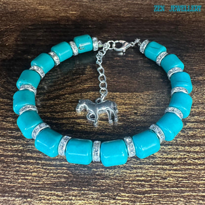 Turquoise tube bead bracelet with sparkly rhinestone spacers and a silver horse charm. Vibrant blue stones and silver extender chain shown against a wooden background. Bracelet displayed on a wood table