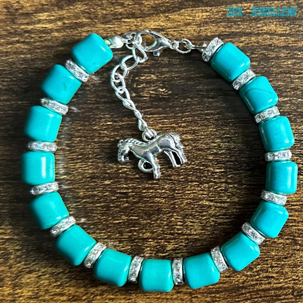 Bright turquoise gemstone-style bracelet photographed on wood to show the bracelet scale and fit, featuring silver clasp details, rhinestone separators, and a dangling horse charm with realistic engraved details.