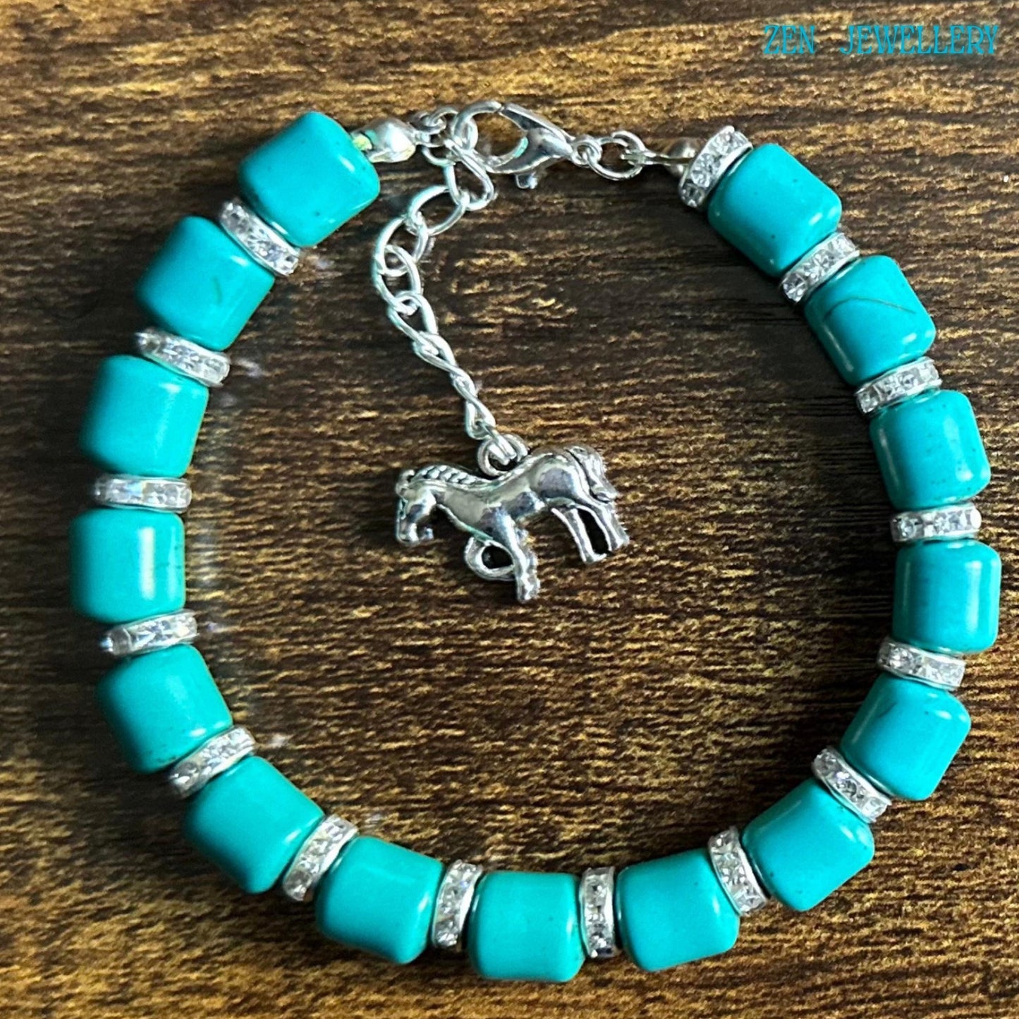 Bright turquoise gemstone-style bracelet photographed on wood to show the bracelet scale and fit, featuring silver clasp details, rhinestone separators, and a dangling horse charm with realistic engraved details.