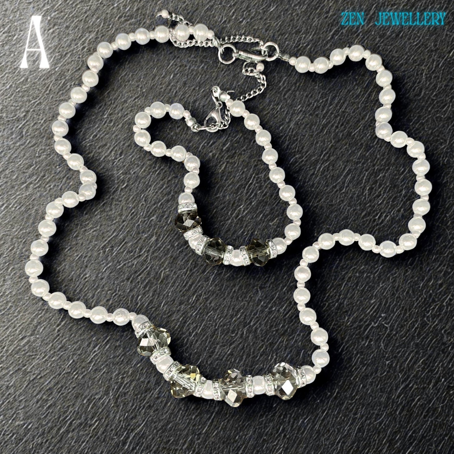 Close-up image of a handmade white pearl jewellery set with faceted grey crystal beads and silver spacer details. The glossy pearl beads reflect light beautifully and create a soft luxurious appearance. The bracelet perfectly matches the necklace and includes sparkling rhinestone spacers that add elegant shine and contrast. The dark background enhances the brightness of the pearls and the sparkle of the crystals.