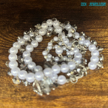 Elegant white pearls necklace and bracelet set with Austrian transparent crystal drops arranged on a dark textured background, creating a luxurious contrast and highlighting the soft shine of the pearl beads.