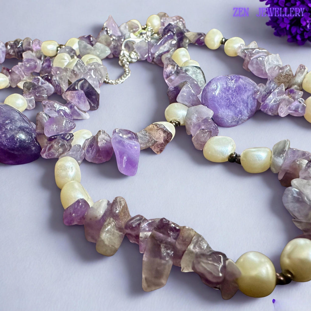 The natural amethyst crystal chips display mixed lavender, violet, and translucent tones with raw organic textures that reflect light softly. Cream pearl-style beads add balance and elegance inspired by classic boho gemstone jewellery collections.