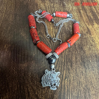 Rustic jewellery flat lay showing handmade genuine coral necklace with polished silver tiger pendant and rhinestone embellishments. The natural red coral beads feature uneven organic textures and rich red colour variations enhancing the artisan handmade aesthetic. The necklace combines bold gemstone styling with modern silver chain elements.