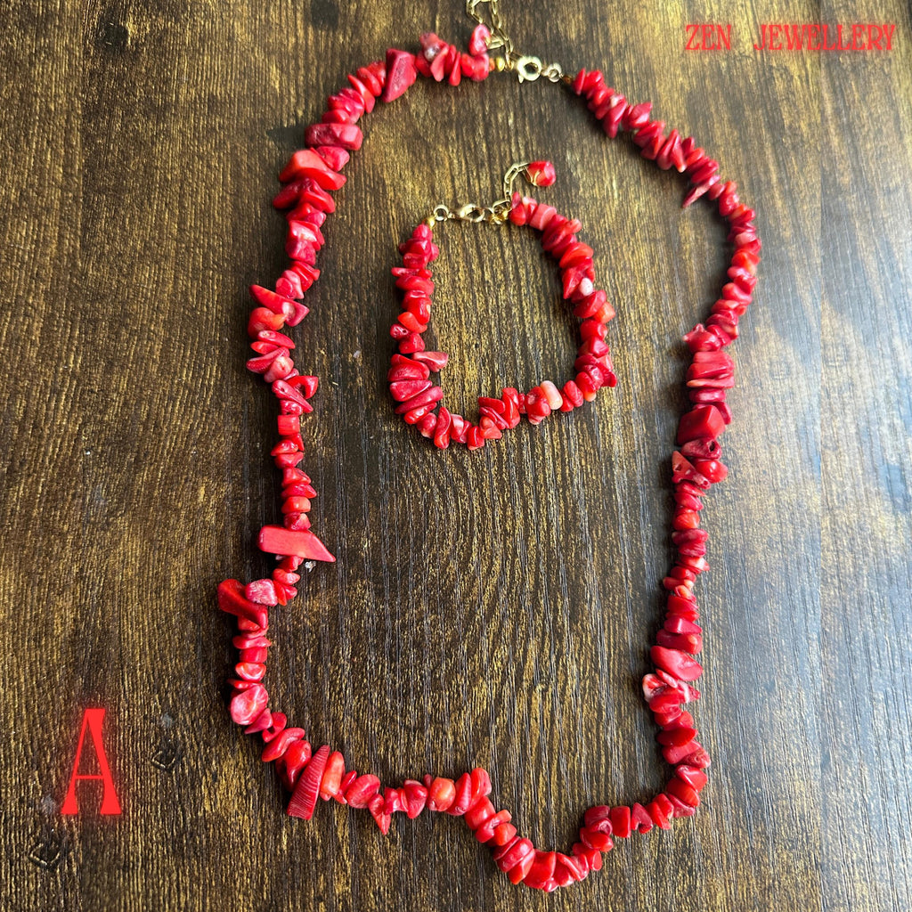 Full jewellery set photograph featuring vibrant coral-red chips with larger bold coral accents connected by gold chain sections and finished with polished gold clasps. The organic shapes of the coral beads create a natural bohemian aesthetic while maintaining an elegant handcrafted appearance.