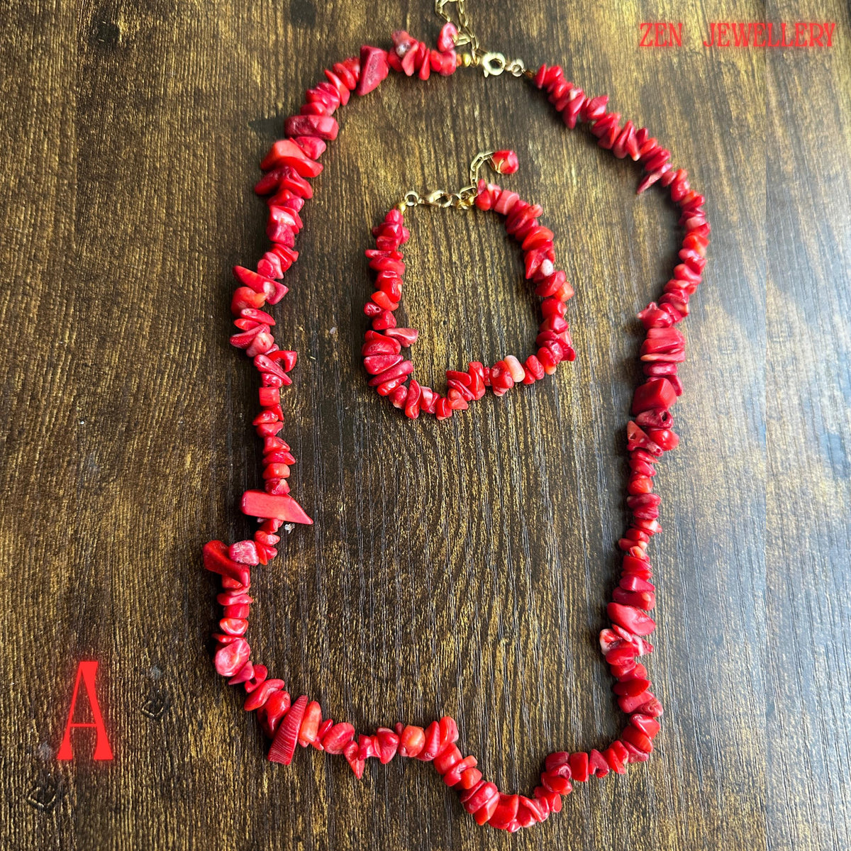 Full jewellery set photograph featuring vibrant coral-red chips with larger bold coral accents connected by gold chain sections and finished with polished gold clasps. The organic shapes of the coral beads create a natural bohemian aesthetic while maintaining an elegant handcrafted appearance.