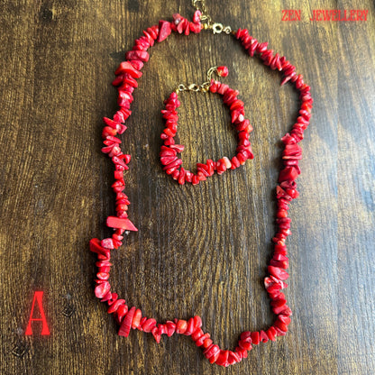 Full jewellery set photograph featuring vibrant coral-red chips with larger bold coral accents connected by gold chain sections and finished with polished gold clasps. The organic shapes of the coral beads create a natural bohemian aesthetic while maintaining an elegant handcrafted appearance.