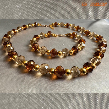 Glamorous handmade necklace and bracelet set featuring faceted amber crystal beads in warm caramel and honey shades combined with metallic gold spacer beads for an elegant evening jewellery look. The jewellery appears lightweight, feminine, and perfect for formal fashion styling or festive occasions.