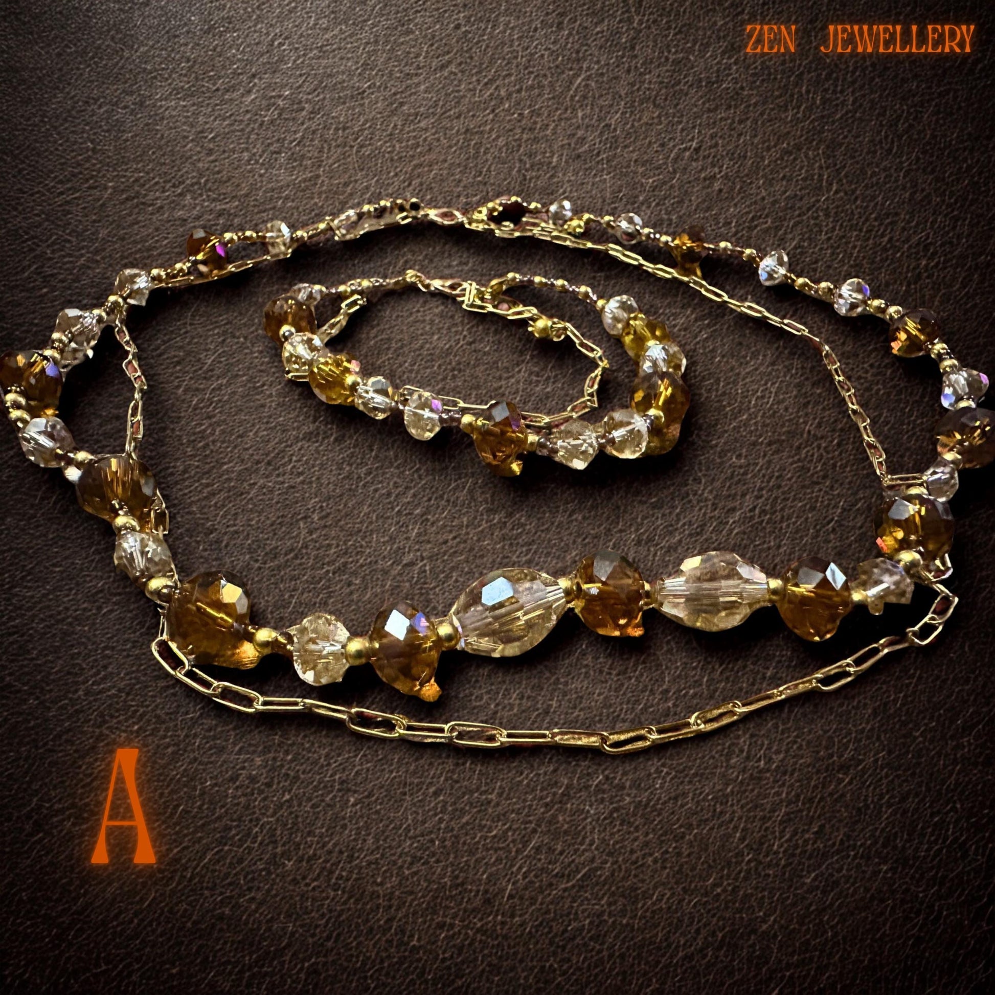 Handmade crystal jewellery set displayed on soft beige fabric featuring sparkling champagne and amber toned Austrian crystal beads. The warm golden colour palette creates an elegant glamorous appearance while the polished gold chain and spacer beads add contrast and sophistication. The lightweight layered necklace and matching bracelet create graceful movement and feminine style perfect for formal outfits or elegant everyday fashion.