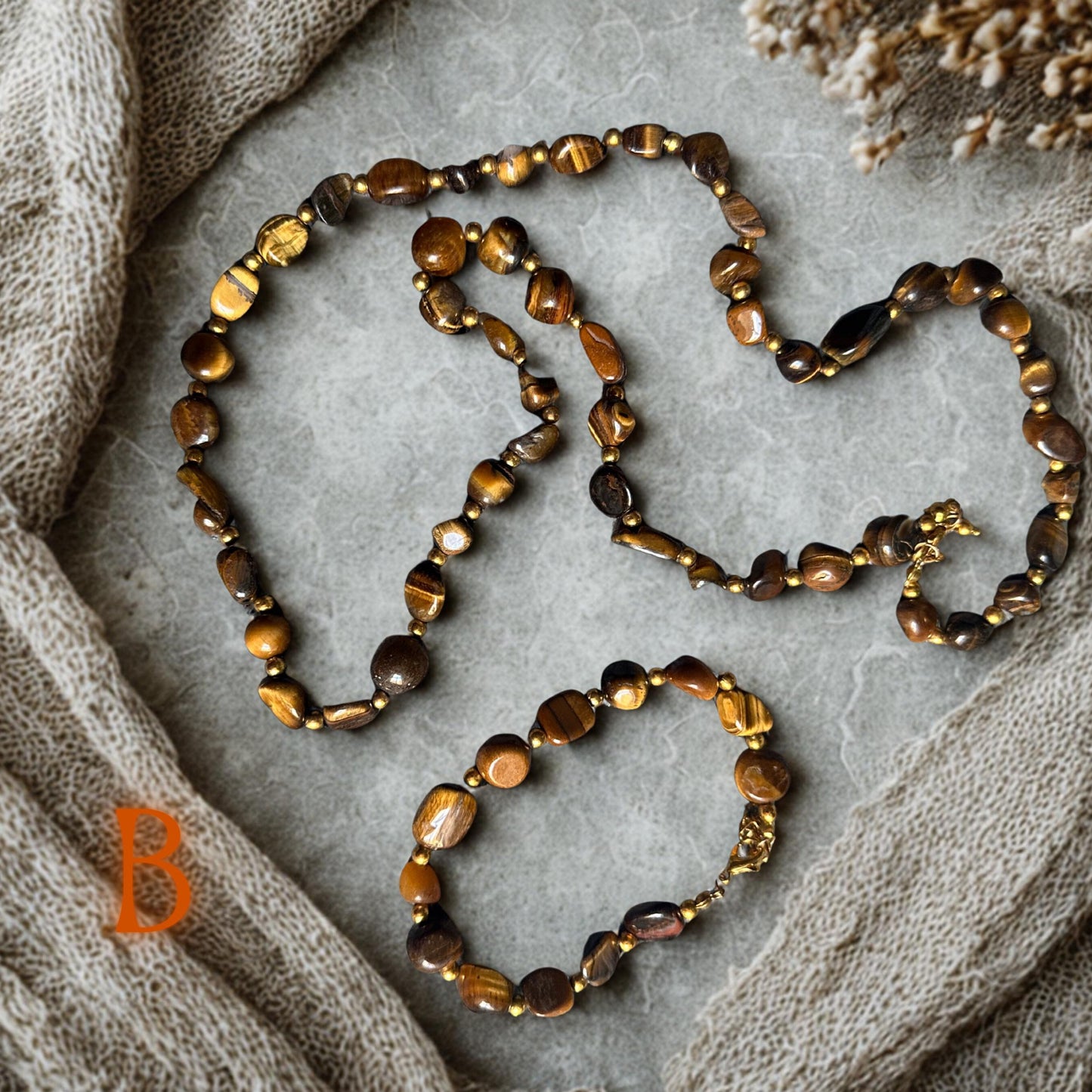 Tiger eye gemstone necklace featuring polished caramel and brown stones with golden reflections styled together with a matching bracelet on a marble background. The warm earthy palette creates an elegant boho fashion look inspired by natural gemstone jewellery.