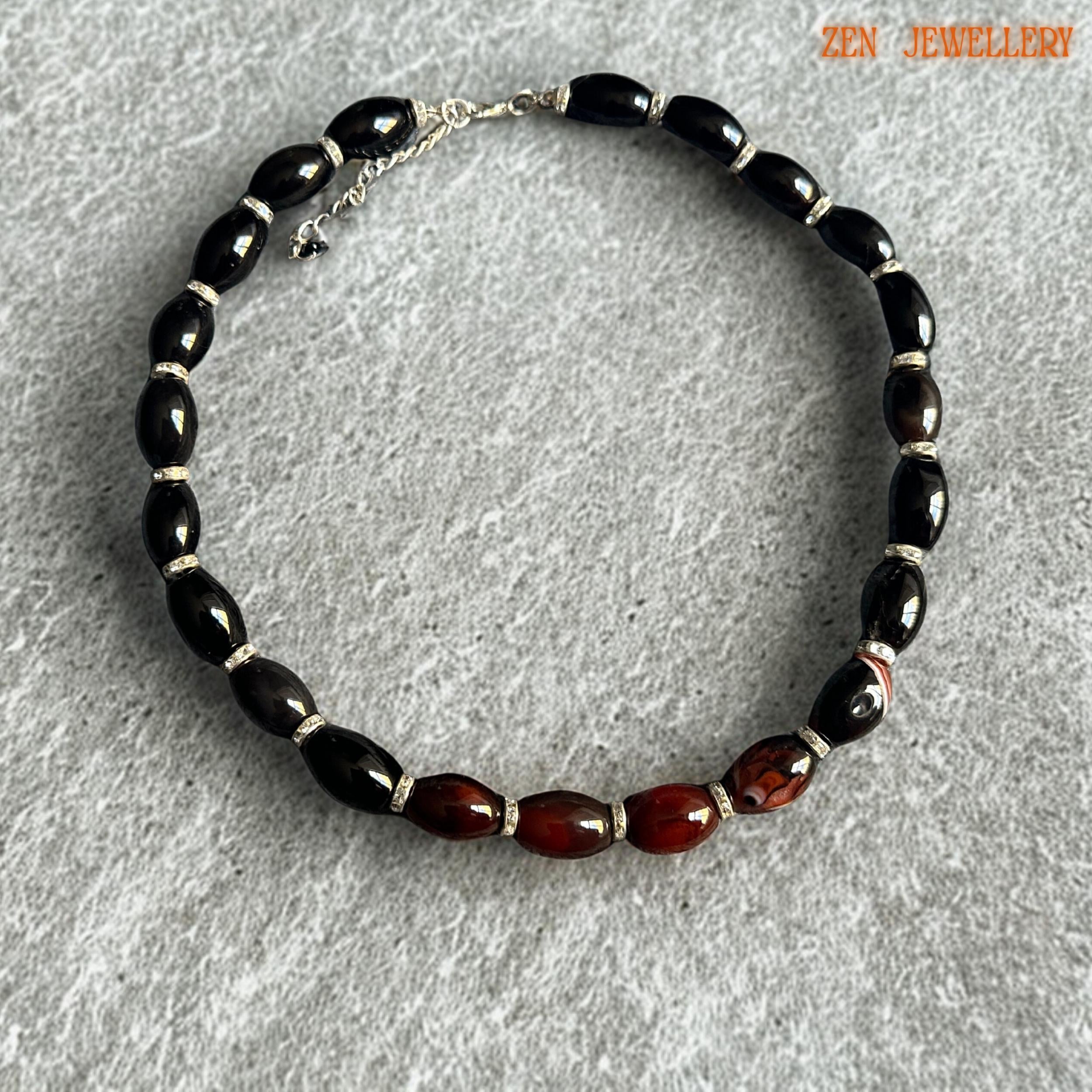 Luxurious AGATE GEMSTONE jewellery necklace featuring polished black oval beads paired with dark burgundy striped agate stones and silver rhinestone spacers. The reflective gemstone surface creates rich shine and dramatic contrast against the soft neutral background. Silver lobster clasp and extension chain allow adjustable sizing and secure wear. Necklace measures approximately 47 cm or 18.5 inches long for comfortable, elegant styling.