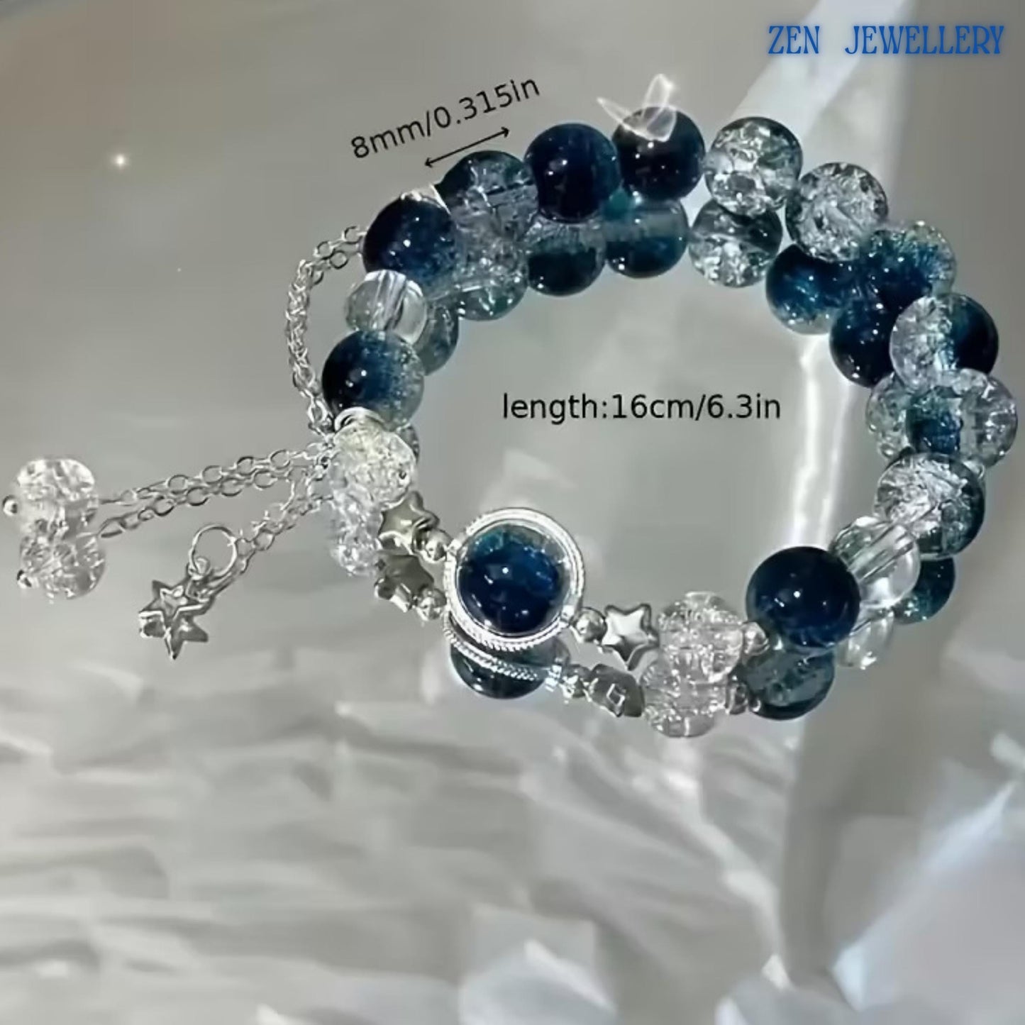 Bracelet photographed from above showing the complete arrangement of deep blue gemstone beads, transparent crackle crystal beads, silver decorative spacers, and dangling chain accents. The combination of glossy and textured surfaces creates beautiful contrast while capturing the calming colours of the ocean and the sparkle of starlight.