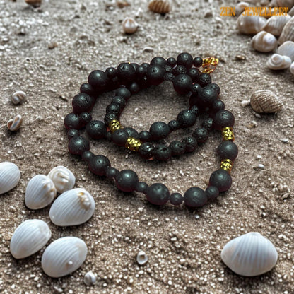 Handmade black lava bead necklace with natural volcanic texture and elegant golden artisan spacer details. The necklace combines multiple bead sizes to create visual movement and balance while maintaining a calming and grounding appearance. The warm gold chain extension and clasp complete the refined, handmade look and add adjustable comfort for styling versatility.