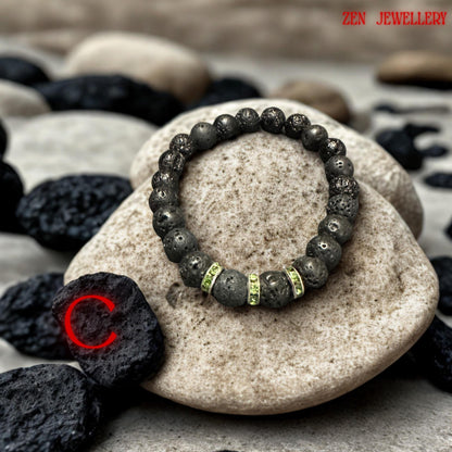 Natural lava stone bracelet with mixed volcanic bead sizes arranged symmetrically around bright green crystal spacer rings. The bracelet has grounding earthy texture with subtle sparkle details and modern handmade design. The dark matte beads create elegant contrast against the vivid rhinestone accents.