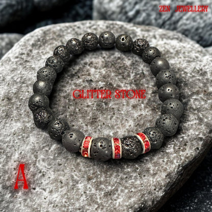 Black lava stone bracelet photographed on stacked smooth grey pebbles creating a calming spa-inspired background. The volcanic beads have natural porous texture with earthy matte appearance while the red rhinestone spacers add elegant sparkle and contrast. The handmade bracelet feels modern, grounding, and stylish.