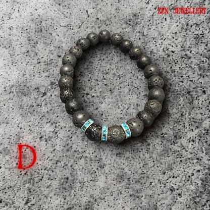 Black porous lava stone bracelet with elegant turquoise crystal spacer accents displayed on smooth spa pebbles, creating relaxing, zen-inspired styling. The handmade bracelet combines organic volcanic texture with modern bohemian elegance and subtle sparkle.