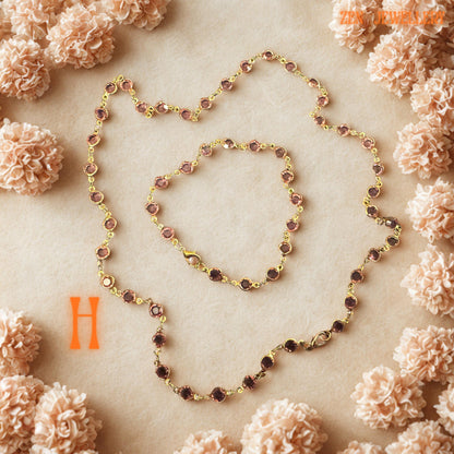 Full necklace and bracelet set displayed in a coordinated flat-lay arrangement with soft floral decoration surrounding the jewellery. The balanced composition highlights the handcrafted artistry, elegant colour combinations, and refined chain detailing across all crystal variations including red, black, blue, and green. The feminine presentation enhances the luxurious romantic feel of the jewellery collection.