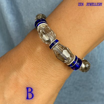 Detailed close-up highlighting the decorative silver ring connectors positioned between clusters of sapphire blue crystal beads. The textured metallic finish adds depth and dimension while complementing the brilliance of the faceted crystals. Sparkling rhinestone accents enhance light reflection across the bracelet. The handcrafted assembly demonstrates careful bead placement, creating a luxurious designer-inspired piece with timeless appeal and