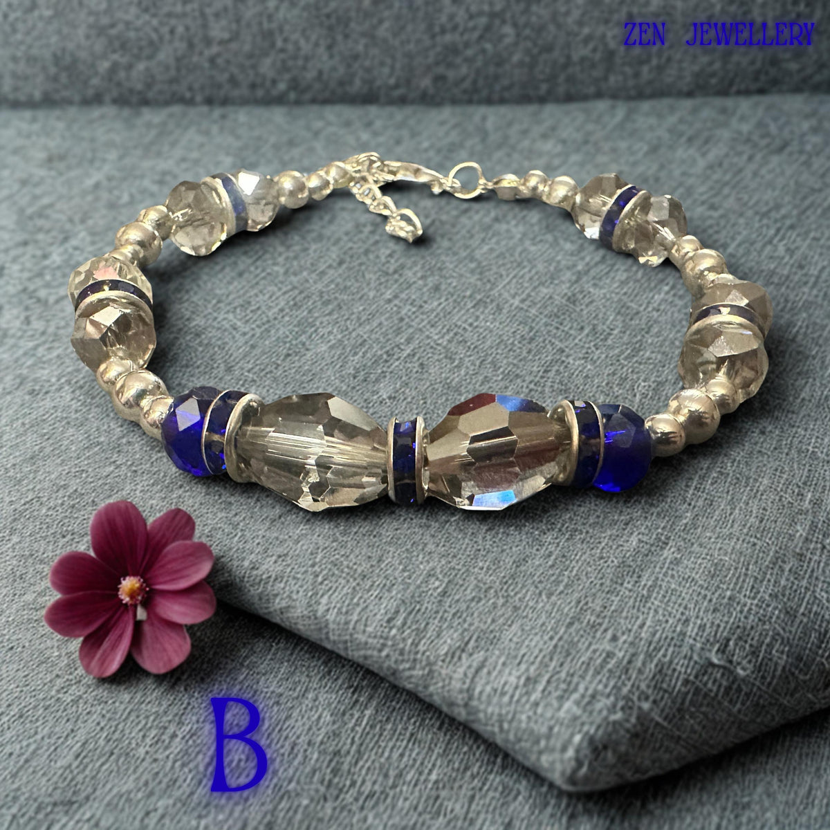 Side-angle image presenting the bracelet clasp area with silver-tone lobster clasp, extension chain, and decorative leaf charm detail. The adjustable fastening allows the bracelet to fit comfortably beyond its standard 17cm length. Small metallic beads transition seamlessly into larger faceted blue crystals, creating a refined and cohesive design. The secure closure system combines practicality with elegant finishing details suitable for regular