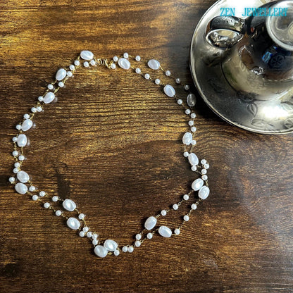 This feminine handmade necklace combines white pearl-style beads in different sizes with elegant golden chain links for a soft luxurious look. The asymmetrical arrangement gives the necklace an organic artistic style inspired by modern boho jewellery and minimalist fashion. The glossy beads create beautiful texture and shine against the dark wooden surface.