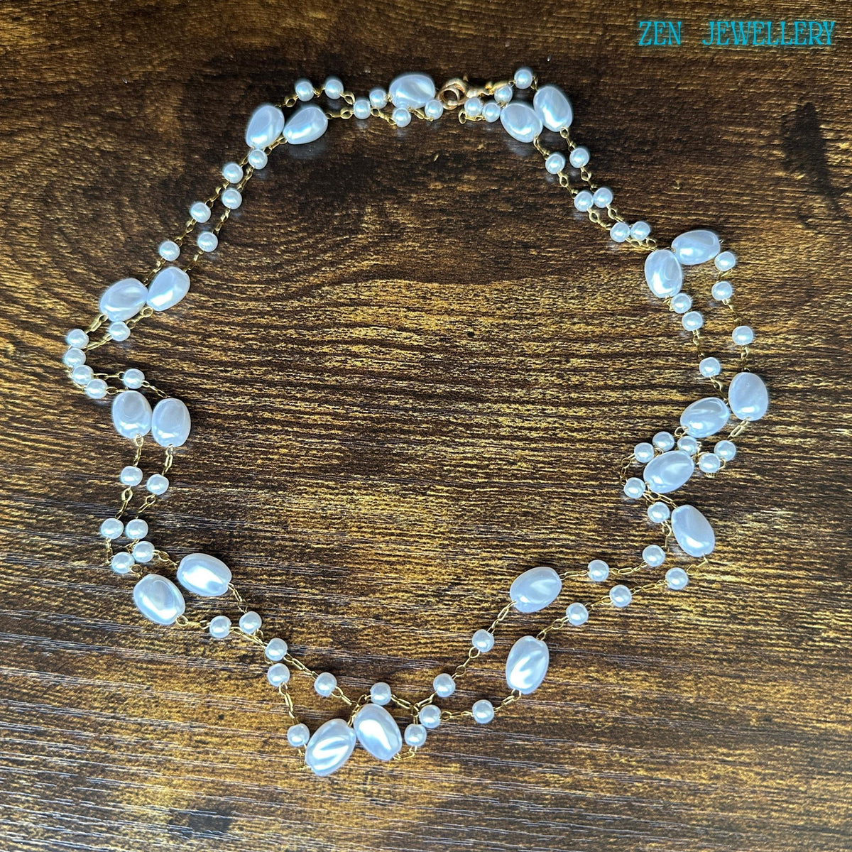 This handmade white bead necklace creates a romantic and timeless look with glossy ivory-style beads and warm gold chain details. The flowing arrangement of beads gives the necklace a layered effect while remaining delicate and refined. The necklace is photographed against a rustic wooden background to highlight the soft white tones and elegant shine.