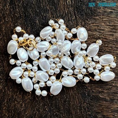 The elegant boho necklace features smooth white oval beads with smaller pearl-style beads carefully linked together using gold chain details. The handcrafted design creates balance and movement with an artistic asymmetrical arrangement. The glossy finish of the beads reflects light softly and adds a luxurious feminine touch.
