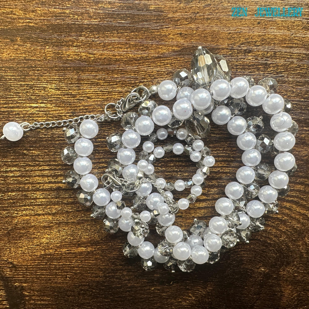 Close view of white pearls necklace featuring sparkling Austrian transparent crystals forming a decorative border along the necklace. Detailed image of a feminine handmade pearl necklace and bracelet set with glossy white beads silver rhinestone spacers and faceted crystal drops. The necklace has a symmetrical flowing design with sparkling crystals placed between the pearls for added brilliance and texture. The bracelet mirrors the same elegant b