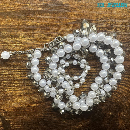 Close view of white pearls necklace featuring sparkling Austrian transparent crystals forming a decorative border along the necklace. Detailed image of a feminine handmade pearl necklace and bracelet set with glossy white beads silver rhinestone spacers and faceted crystal drops. The necklace has a symmetrical flowing design with sparkling crystals placed between the pearls for added brilliance and texture. The bracelet mirrors the same elegant b