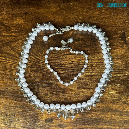 Handmade bridal jewellery set featuring white pearl-style beads paired with shimmering faceted crystals and elegant silver spacer accents. The necklace creates a bold, curved silhouette with dangling crystal details, while the bracelet adds a coordinated, delicate touch. The glossy pearls contrast beautifully against the dark background, and the silver chain closures provide adjustable comfort.