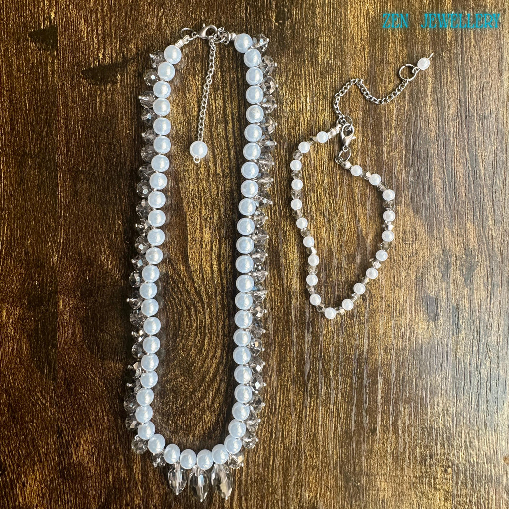 White pearl jewellery set with faceted crystal accents and silver chain clasp displayed in an artistic circular arrangement on a dark textured background. The handmade necklace features luminous pearl-style beads and sparkling champagne-grey crystals that reflect light from different angles creating a glamorous yet timeless look. The matching bracelet adds elegance and balance making the set ideal for bridal wear romantic fashion and special occa
