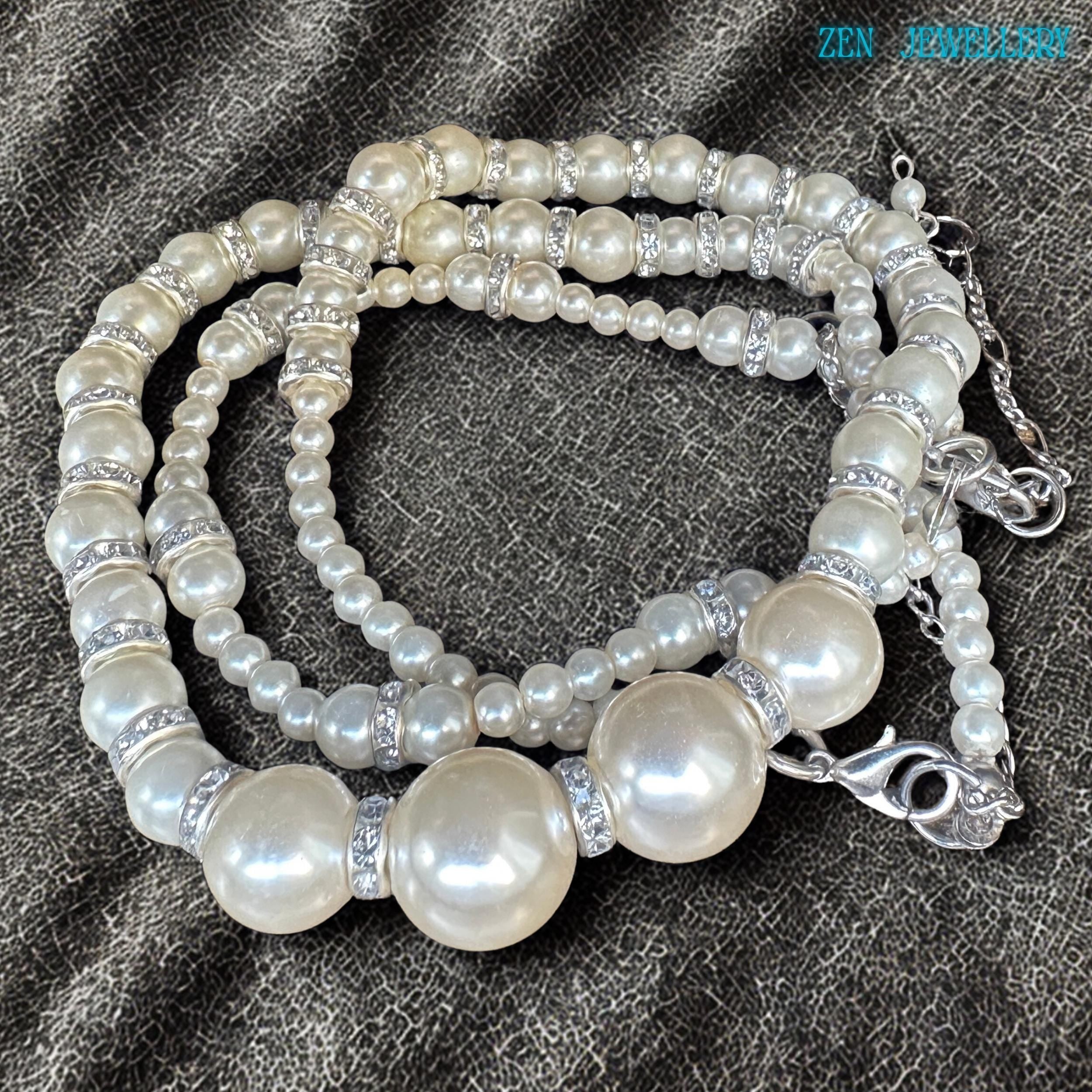 Elegant bridal-inspired necklace and bracelet set featuring glossy pearl-style beads in soft ivory tones combined with sparkling rhinestone spacer accents and silver chain closures. The necklace showcases larger central pearls that create a subtle statement effect while the bracelet provides a delicate matching finish. The reflective pearl surfaces and silver details create a timeless, romantic style inspired by classic pearl jewellery and femini