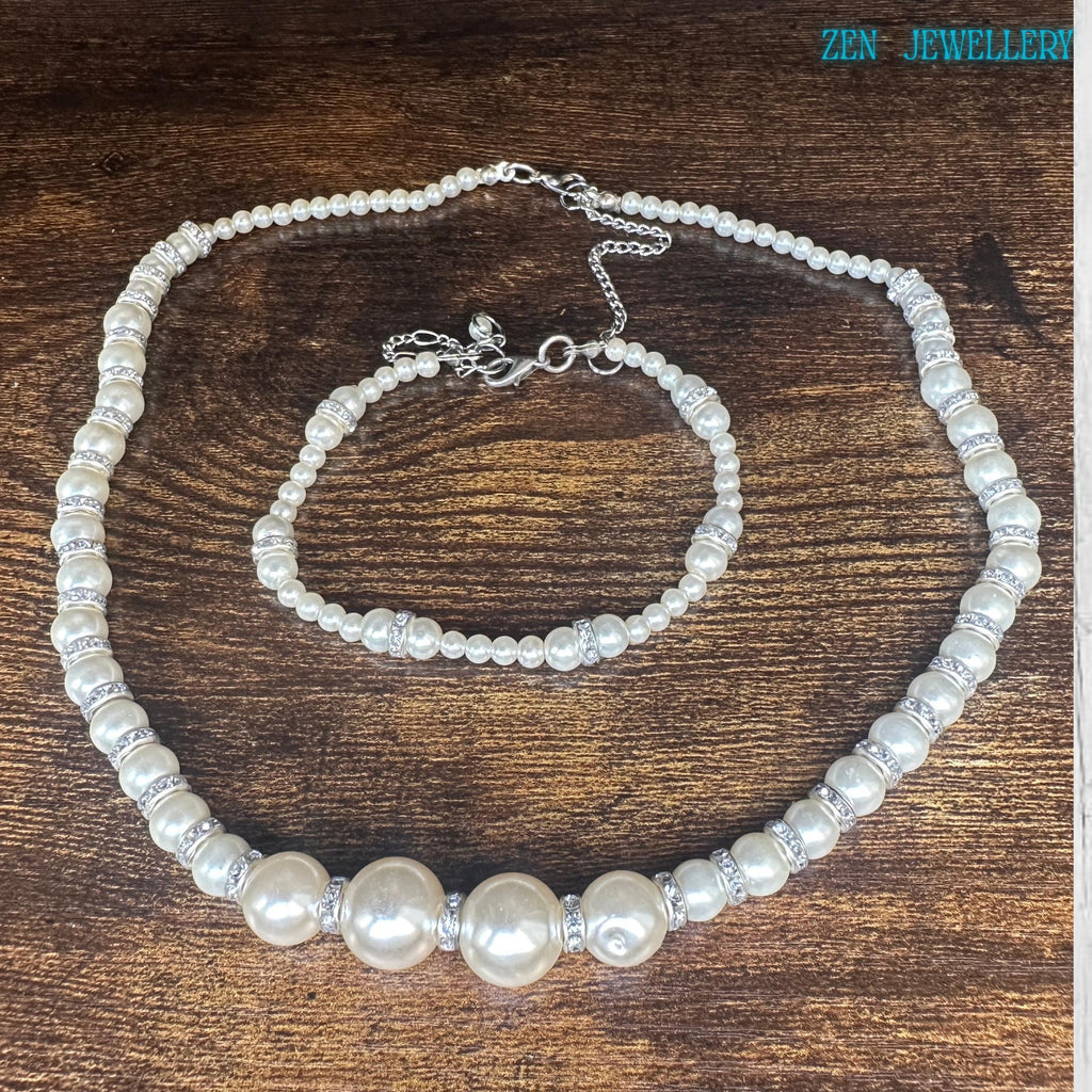 Handmade pearl jewellery set arranged on soft fabric background showing detailed ivory pearl beads silver rhinestone spacers and adjustable silver chain closures. The necklace forms a graceful curved shape with graduated pearl sizes and balanced spacing while the matching bracelet creates a coordinated elegant appearance. The soft cream colours and sparkling accents make this set perfect for brides wedding guests and classic jewellery lovers.