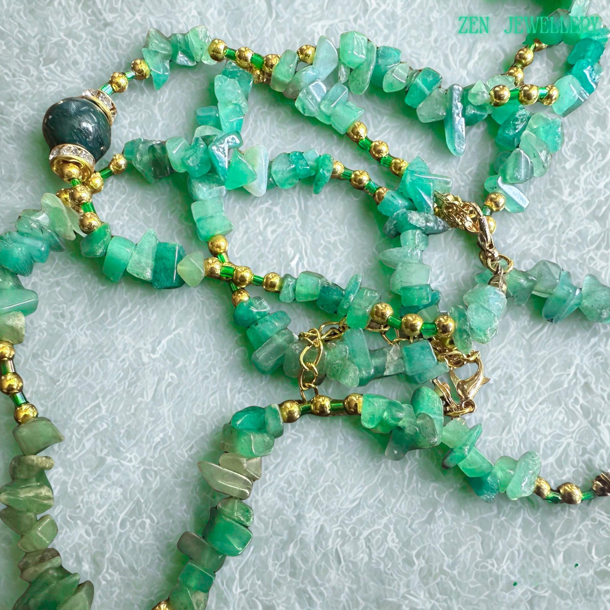 Handmade GREEN AVENTURINE necklace and bracelet set with natural green gemstone chips, gold beads, rhinestone accents, and elegant gold chain details displayed on a soft textured background.
• Close-up view of polished green jade chips mixed with shiny golden spacer beads creating an elegant boho gemstone jewellery design with natural earthy texture and sparkle.