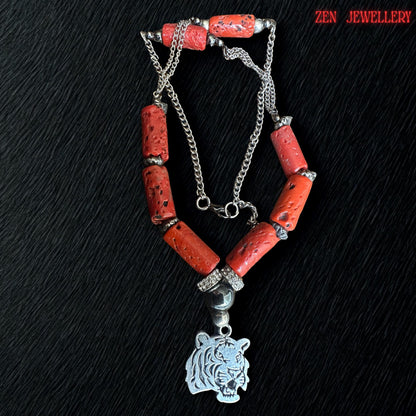 Detailed image highlighting the silver tiger pendant attached to the red coral necklace. The pendant features engraved tiger facial details with polished silver finish beneath black glossy beads and sparkling rhinestone spacers. The surrounding red coral beads show raw organic texture and natural imperfections that enhance the handmade artisan appearance. Necklace length is approximately 22.8 inches.