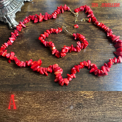 Detailed product image of the red coral necklace and matching bracelet showing polished coral chip textures in different natural shapes and sizes. The larger coral stones positioned throughout the set create contrast and dimension while the gold-tone chain and closures add a refined handmade finish.