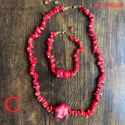 Romantic handmade coral necklace and bracelet set displayed from above showing vibrant red gemstone chips in multiple organic shapes and sizes. The larger coral pieces placed along the centre sections create a balanced statement design while the gold chain adds warmth and elegance.