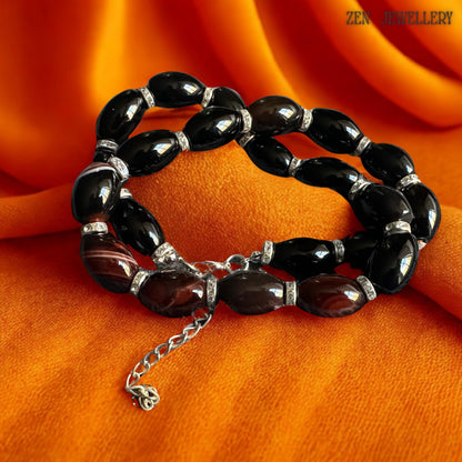 Handmade agate gemstone fashion necklace with large glossy black beads combined with reddish-brown striped accent stones and sparkling rhinestone details. The elegant silver adjustment chain and clasp complete the sophisticated handcrafted design. Soft floral background enhances the feminine luxury appearance of the jewellery. Necklace length is 47 cm equivalent to around 18.5 inches and suitable for statement evening styling.