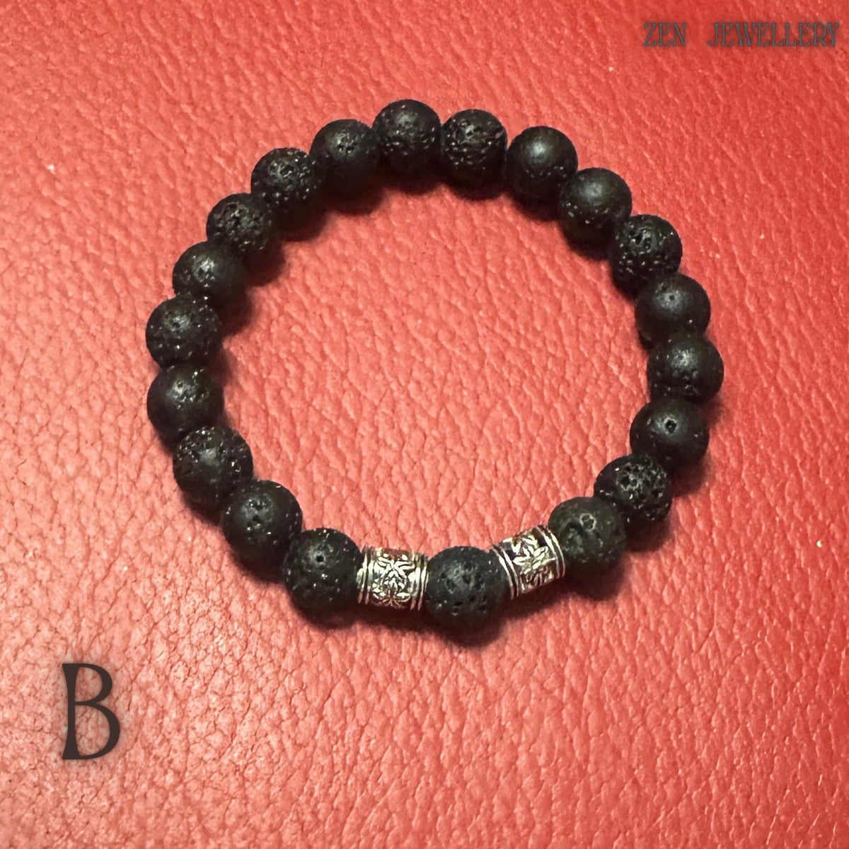 Minimalist black lava stone bracelet photographed on a textured red background to emphasise the deep black volcanic beads and polished silver spacer details. The bracelet features natural porous stones with organic matte surfaces and a handcrafted arrangement. The combination of volcanic texture and silver accents creates a stylish balance between earthy simplicity and refined elegance.