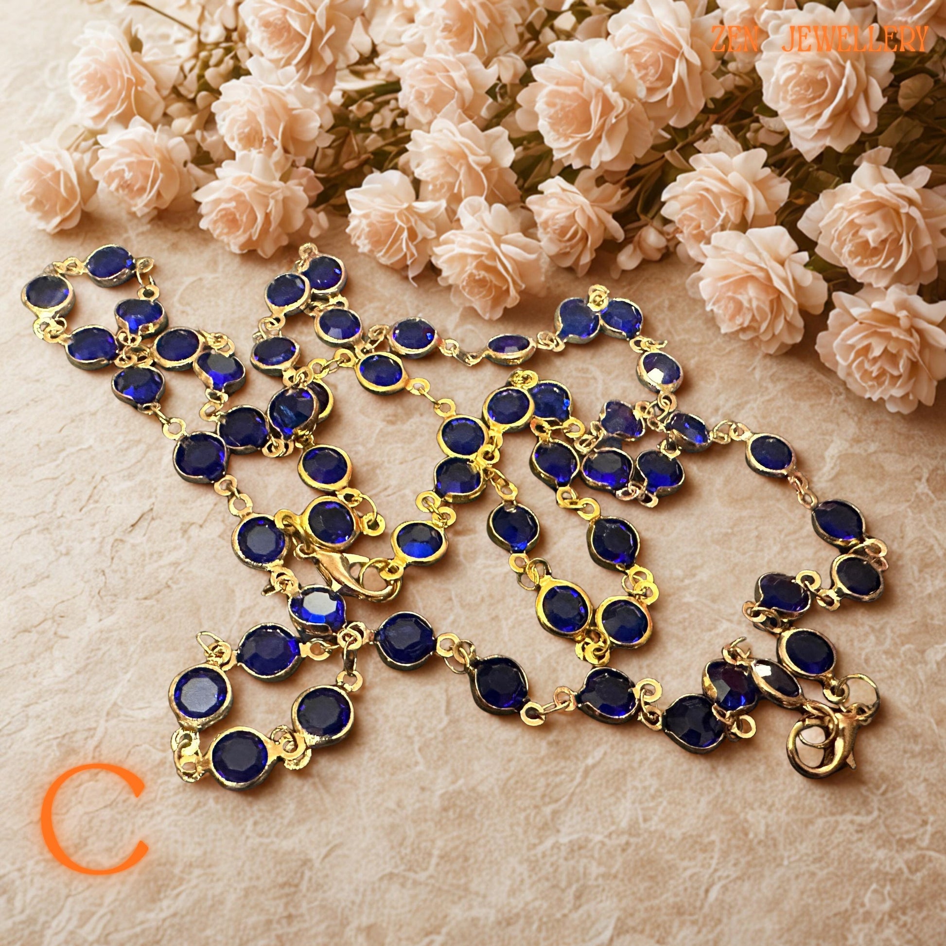 Detailed photograph of the cobalt blue crystal necklace captures the vivid sapphire-inspired tones and brilliant faceted surfaces of the gemstones. The gold-tone chain adds warmth and luxurious shine while the rich blue crystals create celestial beauty inspired by night skies and ocean reflections. The coordinated bracelet complements the necklace perfectly for a complete, elegant jewellery ensemble.