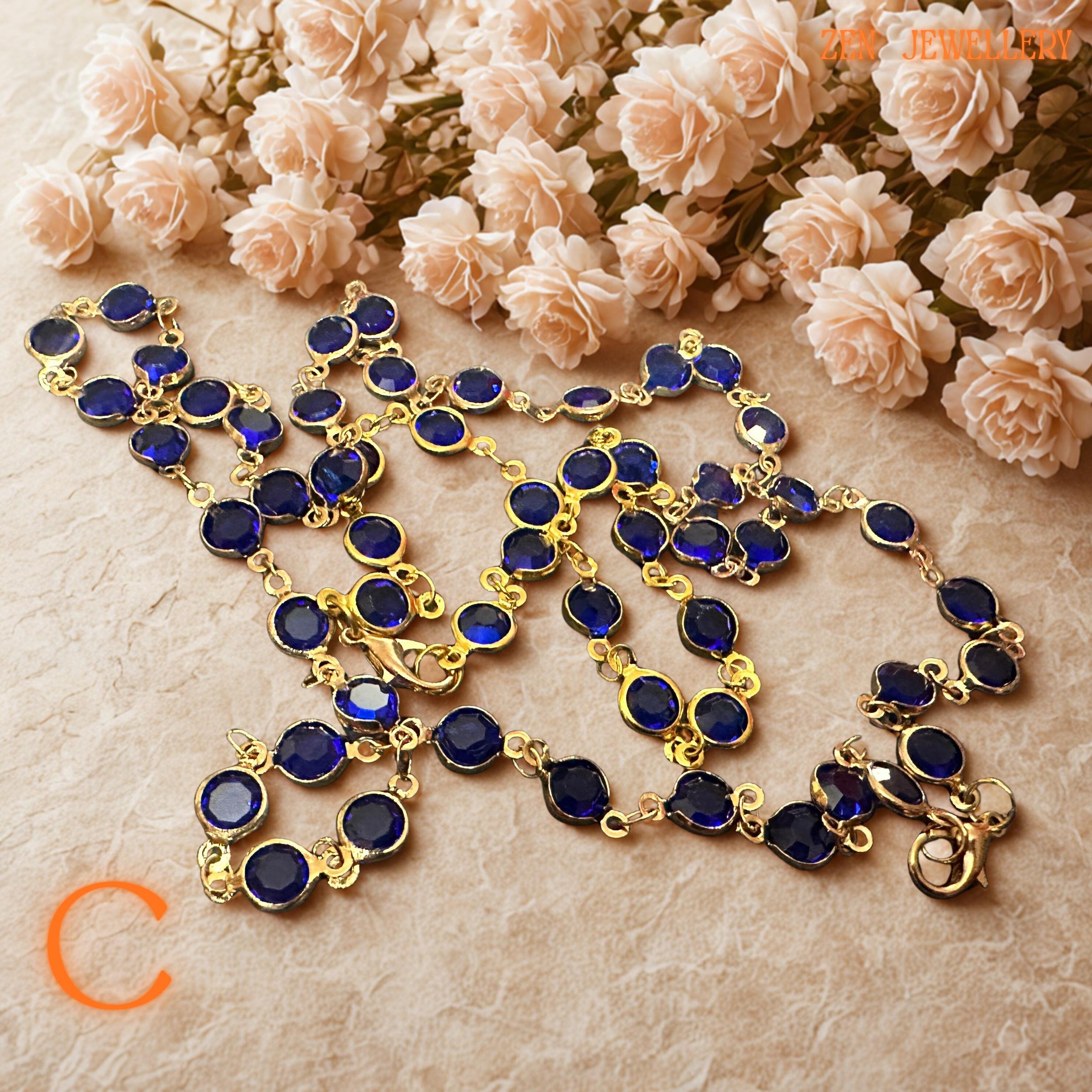 Detailed photograph of the cobalt blue crystal necklace captures the vivid sapphire-inspired tones and brilliant faceted surfaces of the gemstones. The gold-tone chain adds warmth and luxurious shine while the rich blue crystals create celestial beauty inspired by night skies and ocean reflections. The coordinated bracelet complements the necklace perfectly for a complete, elegant jewellery ensemble.