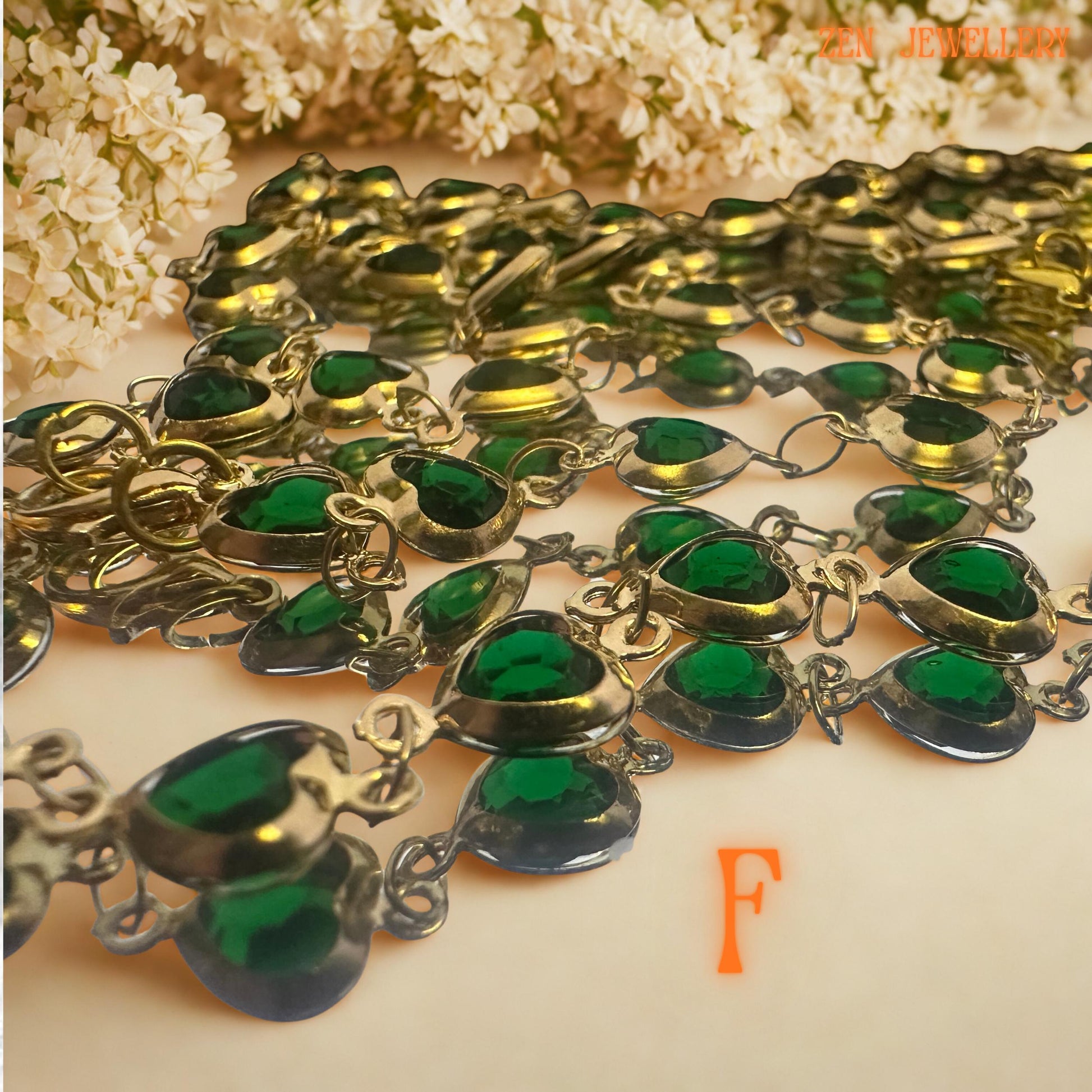 Elegant green crystal jewellery set displayed with soft blush flowers and neutral styling background. Rich emerald green faceted crystals are connected with vintage inspired gold-tone chain and sparkling rhinestone accents for added glamour and texture. The layered artistic design combines botanical elegance with romantic femininity, making this handcrafted necklace and bracelet set ideal for weddings, evening styling, festive fashion, or meaning