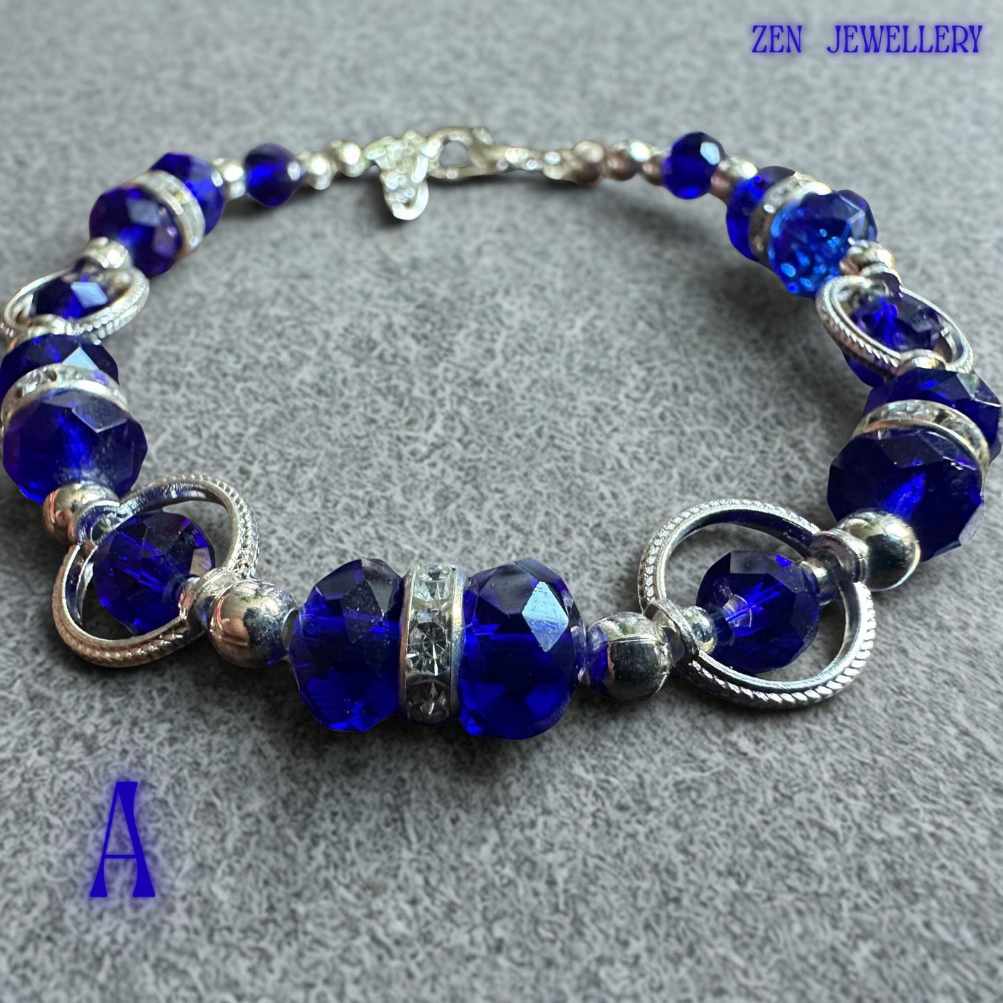 Artistic product image displaying the bracelet against elegant white fabric folds that emphasise the vibrant blue crystal colour. Faceted sapphire-toned beads create dazzling sparkle under light, while decorative silver circles introduce a modern jewellery design element. Crystal rondelles provide additional brilliance and texture. The handcrafted construction is visible throughout the piece, showcasing attention to detail and a balanced arrangem