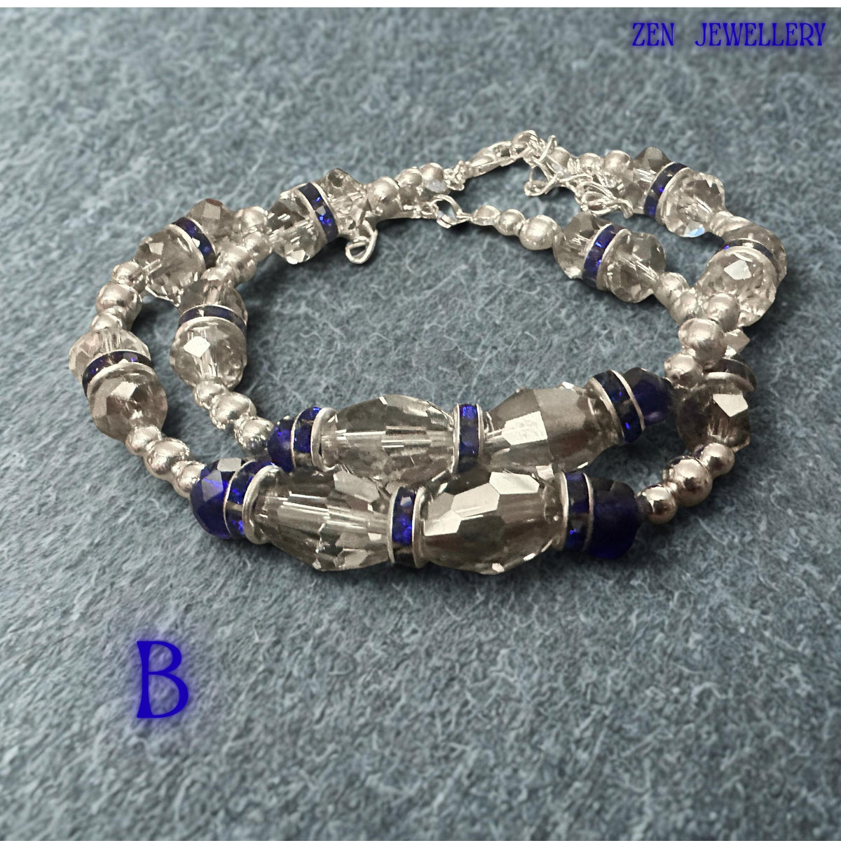 Detailed product view focusing on the central arrangement of deep blue crystal beads separated by sparkling rhinestone spacers. The faceted bead cuts create dynamic reflections and visual movement throughout the piece. Decorative silver-tone rings frame selected crystal sections, enhancing the contemporary style. The adjustable clasp design ensures comfortable wear, while the overall colour palette delivers elegance suitable for both special occa