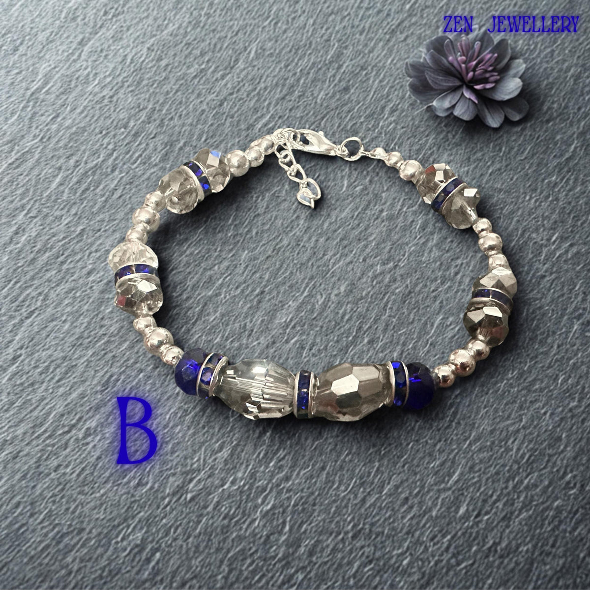 High-resolution photograph capturing the vivid sapphire and royal blue crystal tones against a softly textured fabric backdrop. Faceted crystal surfaces reflect surrounding light, producing brilliant sparkle and colour variation throughout the bracelet. Silver-tone accents and rhinestone rondelles provide luxurious contrast. The balanced symmetrical layout highlights the artisan craftsmanship and thoughtful design that make this bracelet suitable