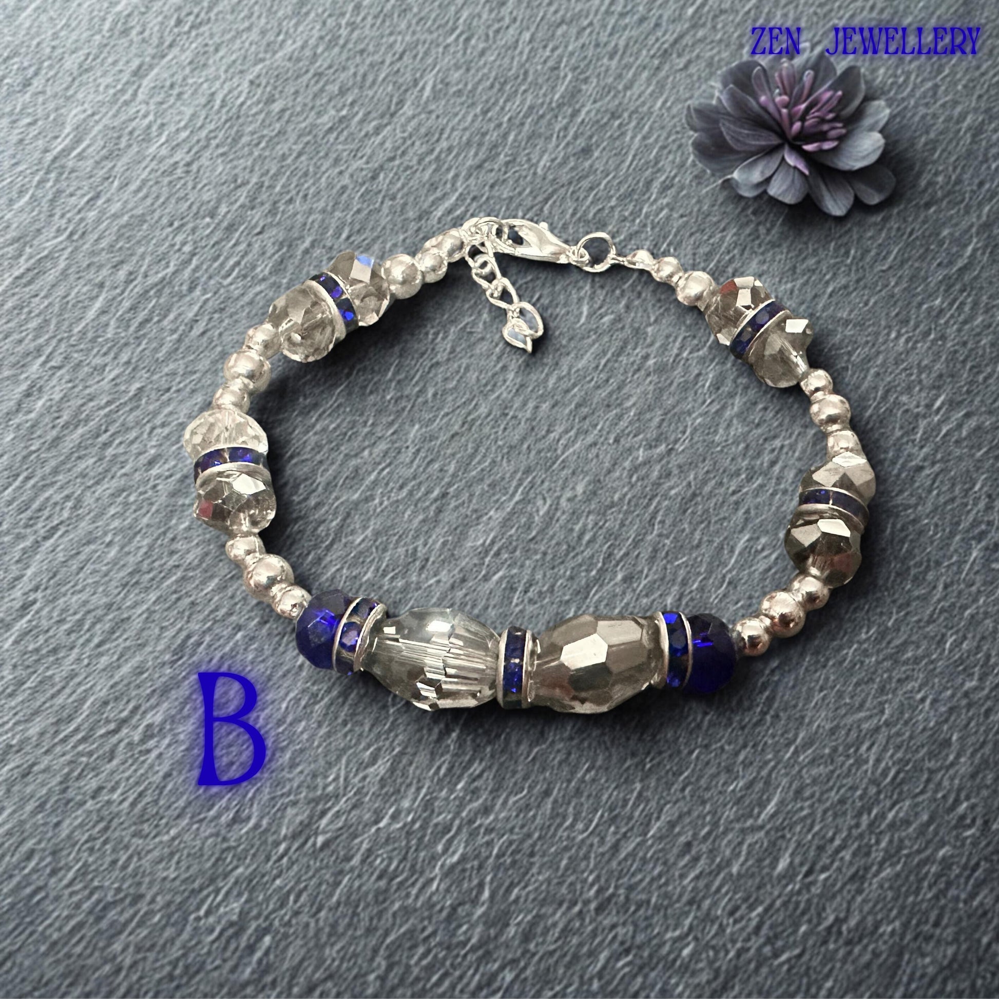 High-resolution photograph capturing the vivid sapphire and royal blue crystal tones against a softly textured fabric backdrop. Faceted crystal surfaces reflect surrounding light, producing brilliant sparkle and colour variation throughout the bracelet. Silver-tone accents and rhinestone rondelles provide luxurious contrast. The balanced symmetrical layout highlights the artisan craftsmanship and thoughtful design that make this bracelet suitable